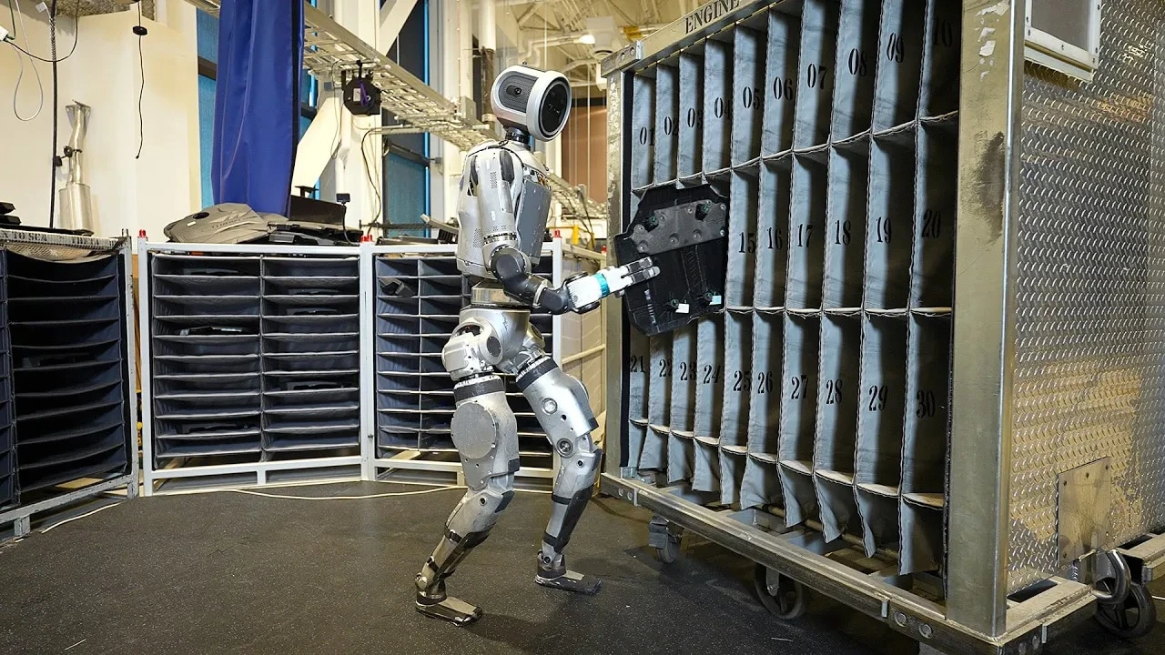 Boston Dynamics 官方图：Atlas 在工业试验场景中转运发动机盖件。
